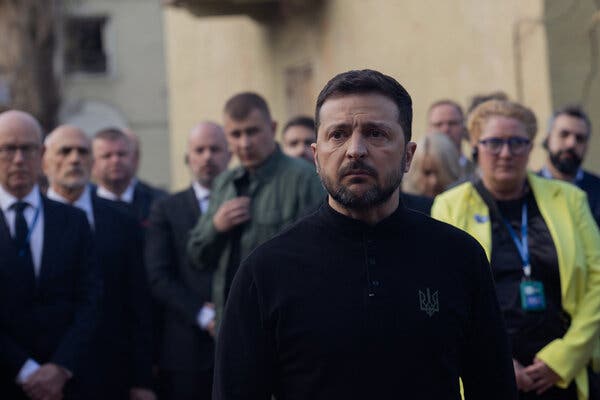 President Volodymyr Zelensky, accompanied by diplomats, stands near a missile-damaged residential building in Kyiv last month.